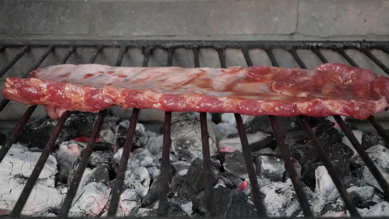 Rack of ribs grilling over hot charcoal with smoke rising, rustic outdoor BBQ vibe