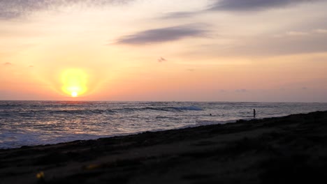 vibrante puesta de sol en la playa de bali con una pareja joven nadando en las olas cercanas