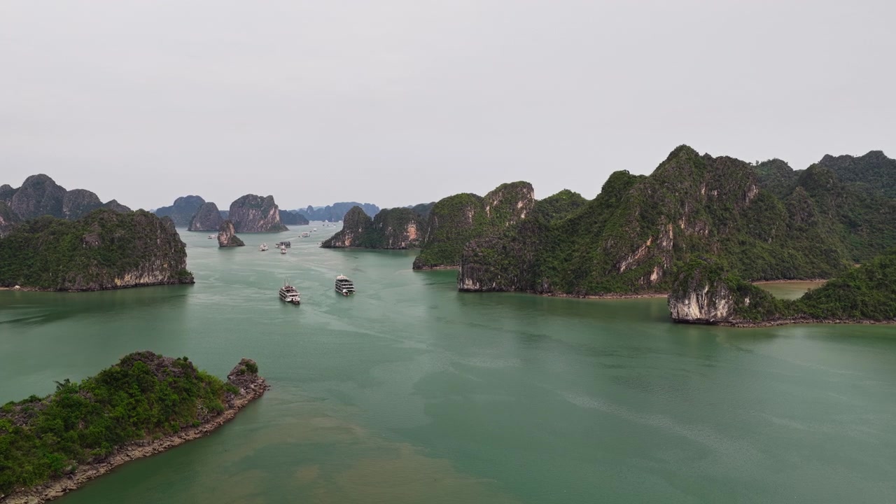 Bay chậm trên không qua làn nước biển xanh ngọc bích và những đỉnh núi đá vôi karst xanh tươi tại Vịnh Hạ Long, Việt Nam.