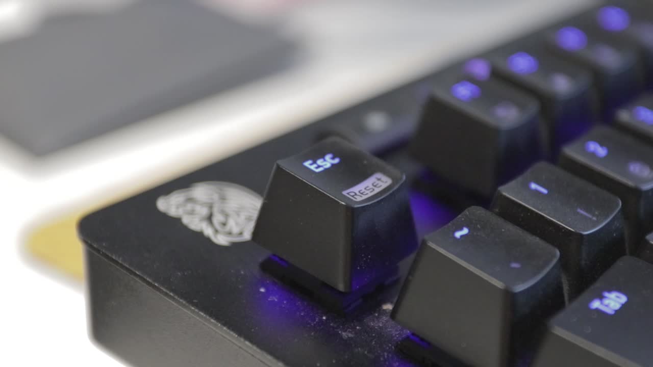 Hand pressing a single key on a slightly dusty, black keyboard with blue backlit keys