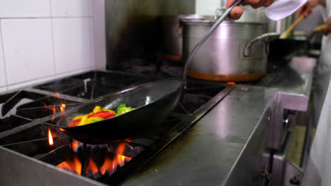 cocinero freyendo verduras en un wok y añadiendo cuchara de agua