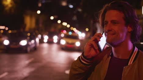 hombre caucásico sonriendo y hablando por teléfono en una calle por la noche