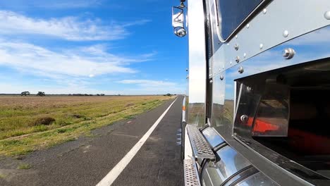 toma tomada desde el costado de un camión hacia la carretera, paisaje con vegetación baja y cielo azul con nubes en el horizonte