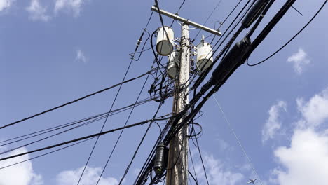 A-low-angle-shot,-looking-up-at-a-typical-utility-pole-on-a-sunny-day,-with-white-clouds-in-a-blue-sky