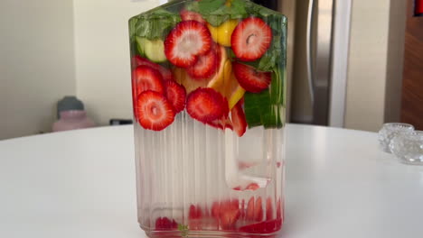 push in on glass pitcher of spa water on tabletop, water infused with strawberries, lemon, and basil