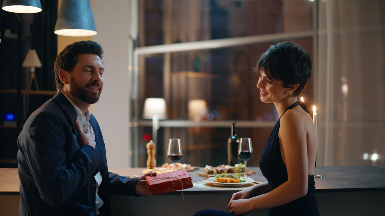 Fidanzata sorridente che fa un regalo durante una serata romantica. Uomo sorpreso che riceve il dono