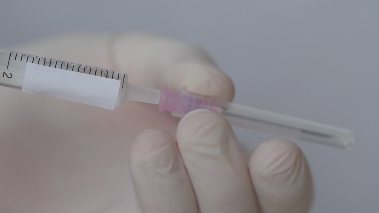 Syringe For Immunization Holding By A Nurse While Putting Needle, Close Up Shot