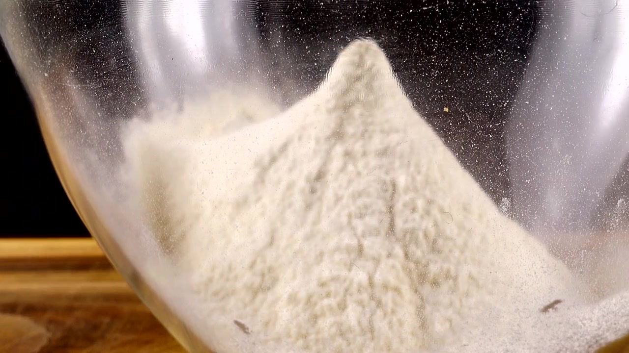 Mengayak tepung menggunakan saringan ke dalam mangkuk kaca di dapur.