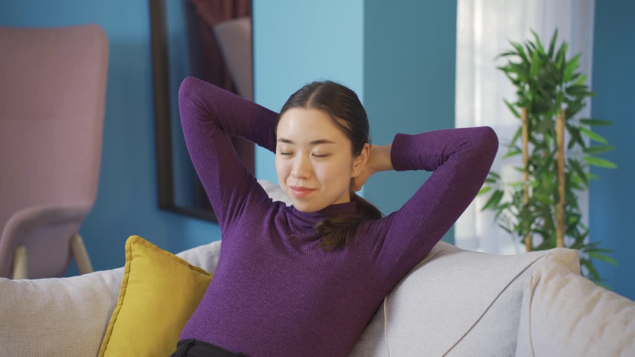 아시아 여성이 거실에서 혼자 앉아서 좋은 분위기로 웃고 있습니다.