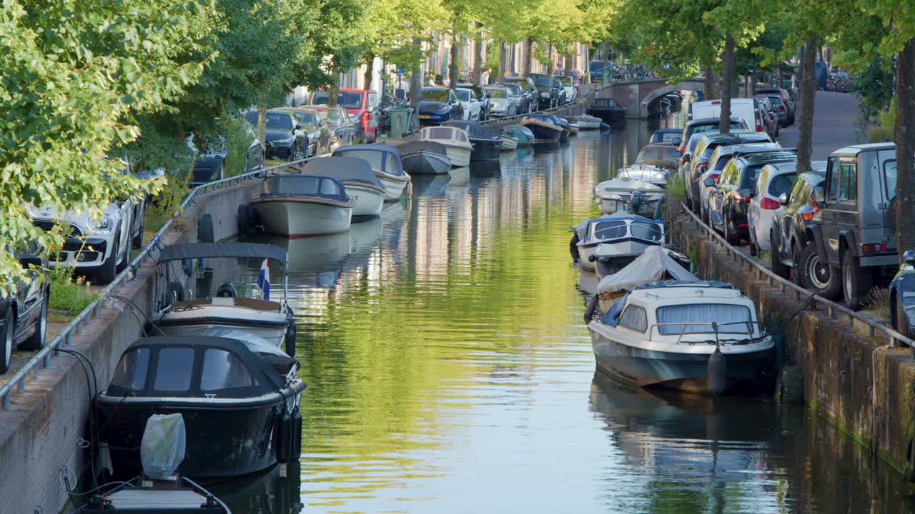 Tranquil summer canal in Haarlem, Netherlands, with moored boats, leafy trees, and gentle movement
