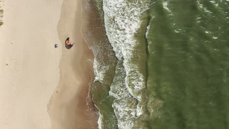 Antena:-Vista-Superior-De-Un-Surfista-Que-Intenta-Levantar-Una-Cometa-De-Viento-Mientras-Está-De-Pie-En-El-Agua-Del-Mar-Cerca-De-La-Playa