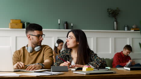 close up view of a student with headphones talking with female mate at table discussing about a project using laptop