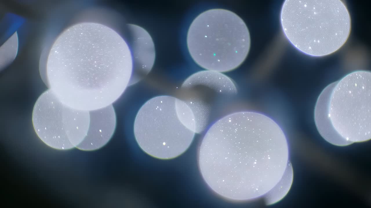 Skiftende klynge av lyskuler ute av fokus som beveger seg etter fokusjustering i et mørkt studio, glitter