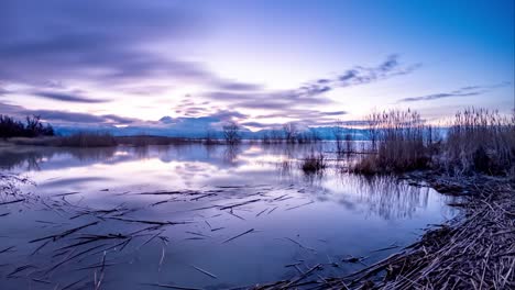 dark to dawn time lapse of a lake with mountains and the sky reflecting off the surface of the water - static wide angle