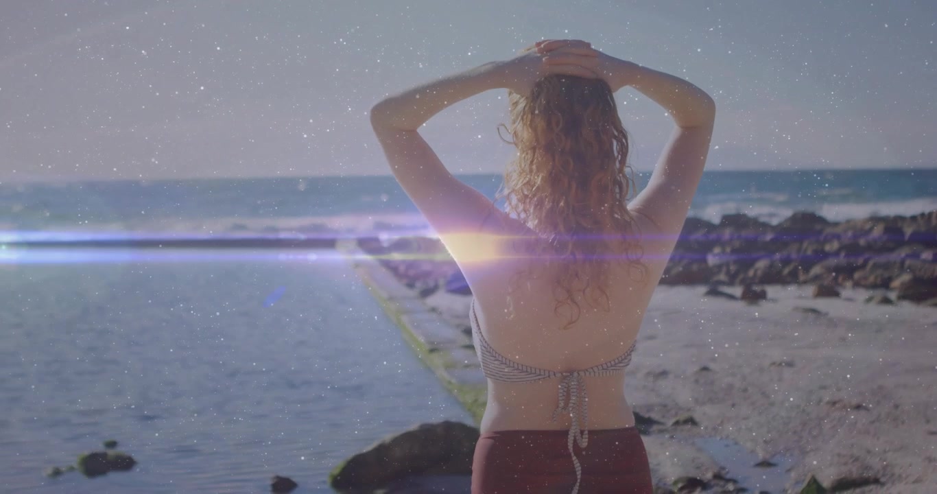Viaje: mujer levantando los brazos a la cabeza, con un destello de lente deslizándose por el mar y una superposición de grano.