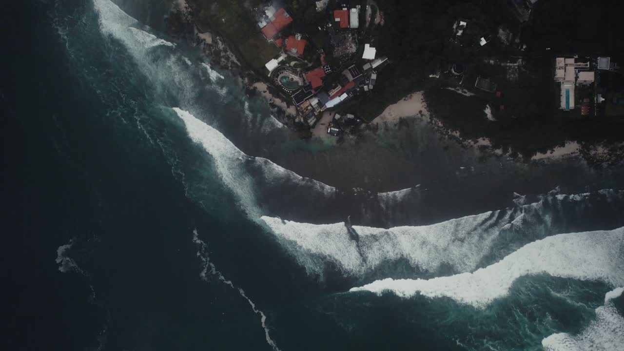 Luftfoto zoom ud fra et surfspot på Bali, Indonesien, med enorme havbølger langs kystlinjen.