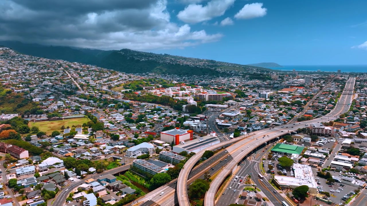 Vasto paesaggio urbano denso della soleggiata Honolulu, Hawaii, USA. Un drammatico cielo grigio nuvoloso avanza sulla città dalle montagne. Prospettiva aerea