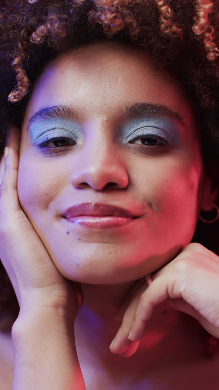 Vertical video of biracial woman with dark hair in blue and pink light, slow motion