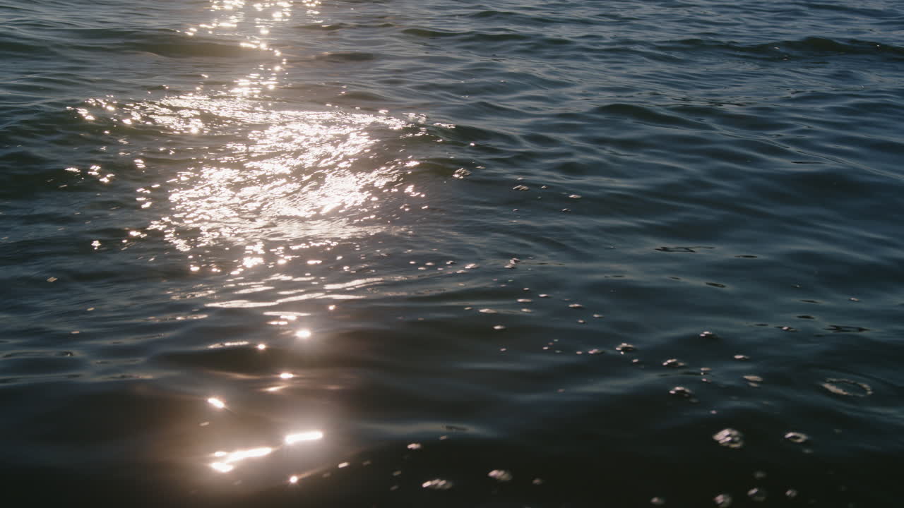 Sunlight reflection glimmering on water during sunset. Gentle waves rolling on a lake. 4K