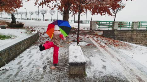 niña pequeña con paraguas de muchos colores juega pateando bolas de nieve