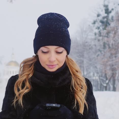 una mujer camina en un parque de invierno usa un teléfono inteligente