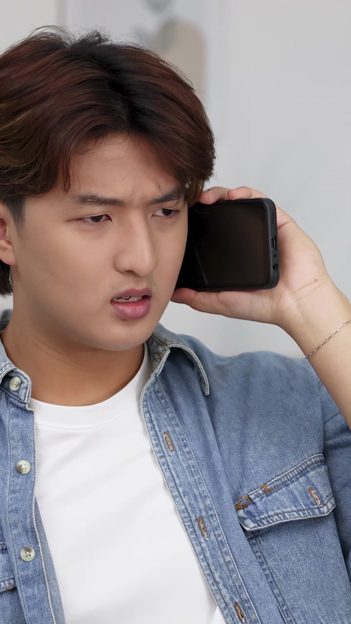 Mezzo busto di un giovane uomo asiatico in camicia di jeans che parla seriamente al suo smartphone