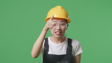 close up of asian woman worker wearing goggles and safety helmet shouting to camera while standing in the green screen background studio