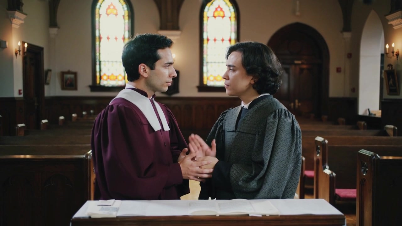 Dois clérigos de mãos dadas, vestindo vestes marrom-acinzentadas, realizando uma bênção no altar, com a cerimônia começando.