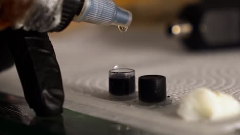 slow motion close up handheld shot of a tattoo artist adding clear ink to small containers full of blank ink to create a grey color for shading to prepare for a client session