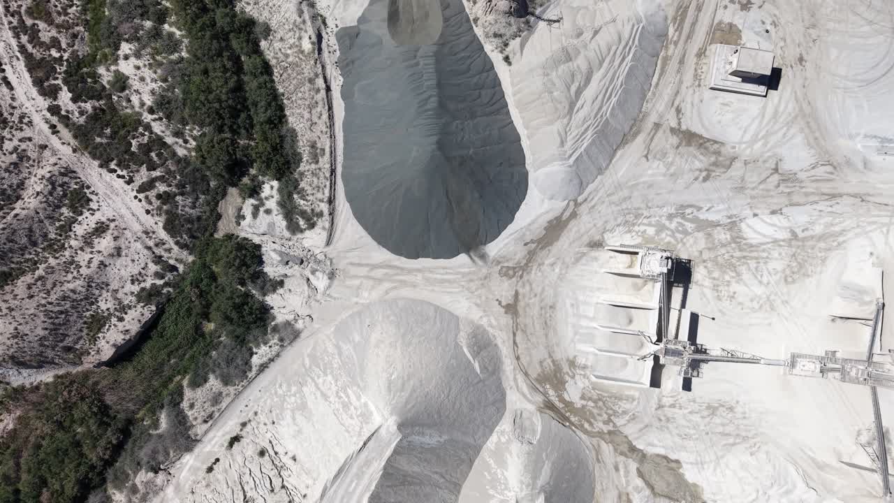 A tracking drone shot from a top-down perspective showing a gravel business with massive piles of aggregate, trucks, and processing machinery