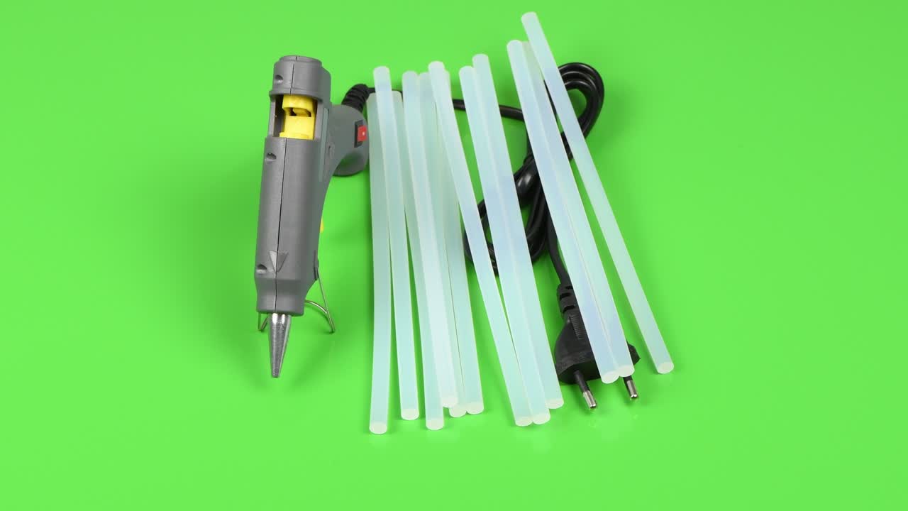 pistola de pegamento eléctrico caliente y palo de silicona aislados en verde. vista lateral. movimiento de bucle. rotación 360.