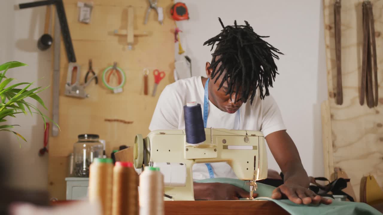Focused african american craftsman with dreadlocks using sewing machine in leather workshop