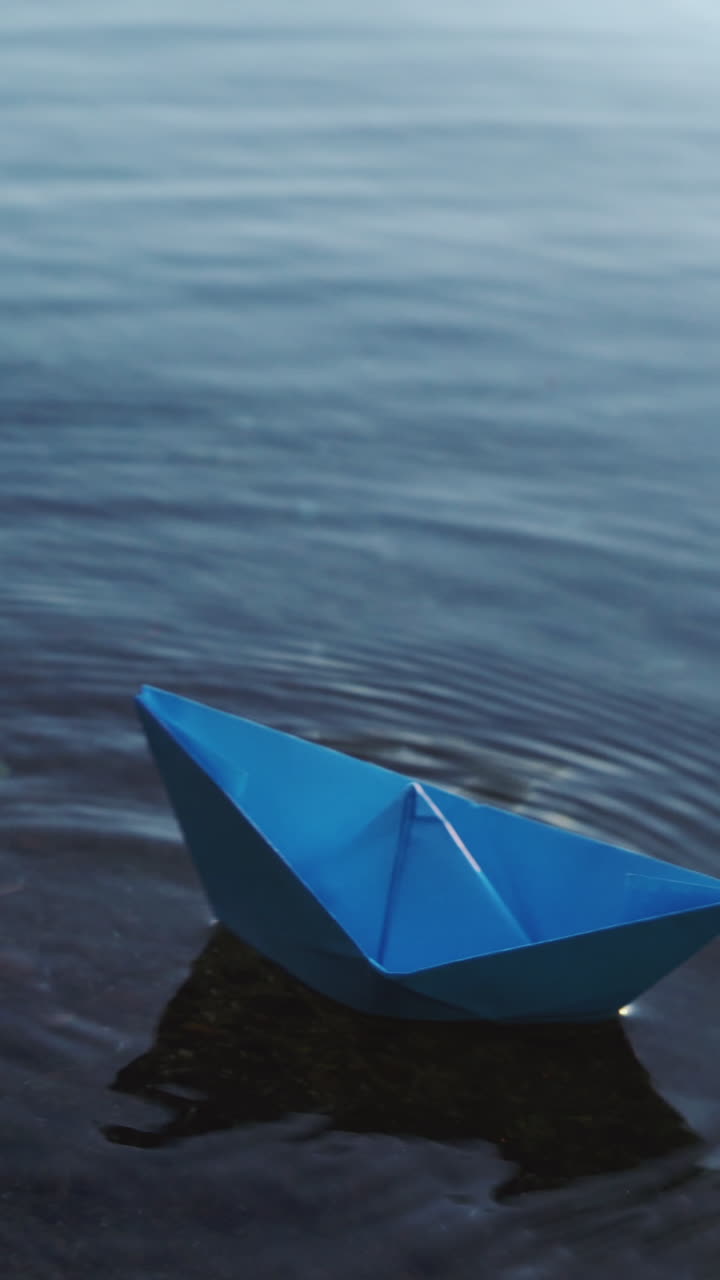 Paper ship in children hand. Blue paper ship. Beautiful sunset Vertical video