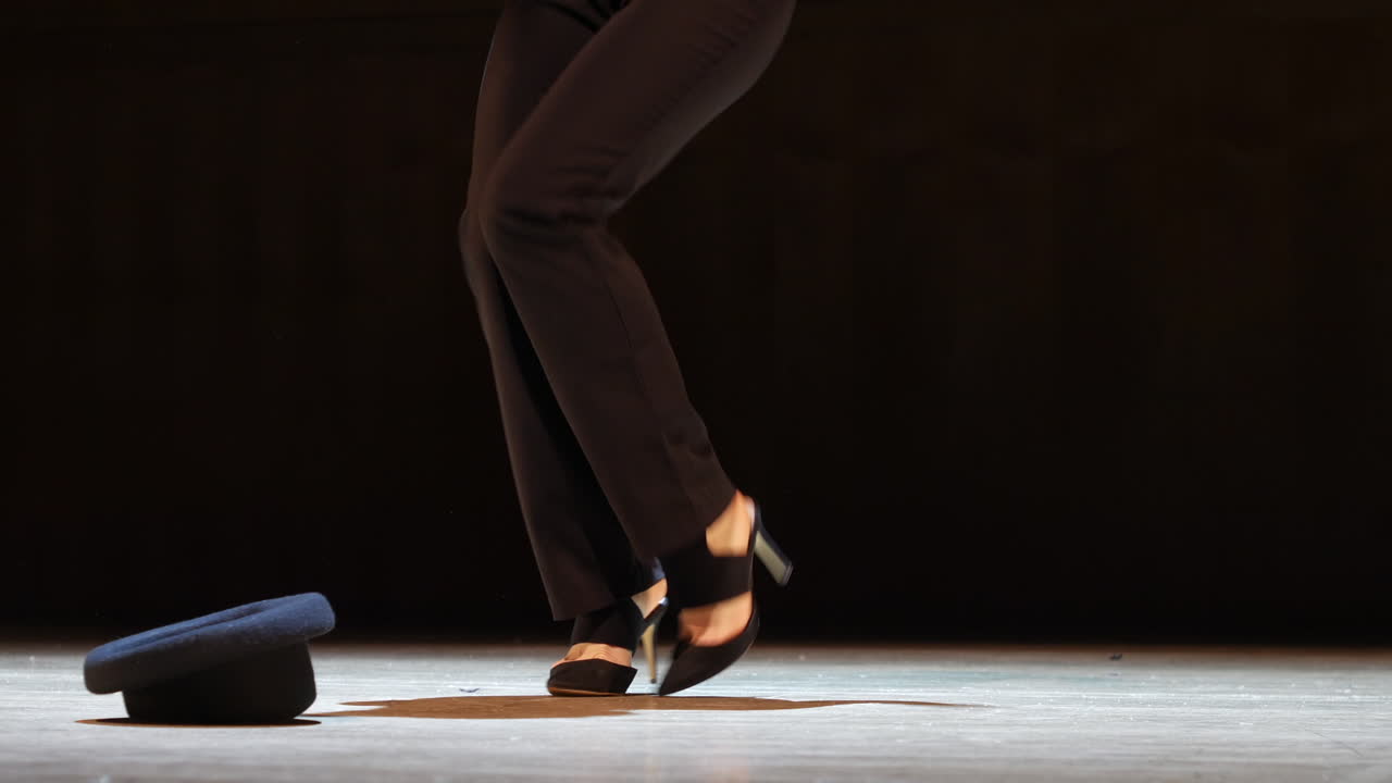Unrecognizable woman dancing on stage in spotlight with bowler hat on the floor