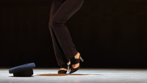 unrecognizable woman dancing on stage in spotlight with bowler hat on the floor