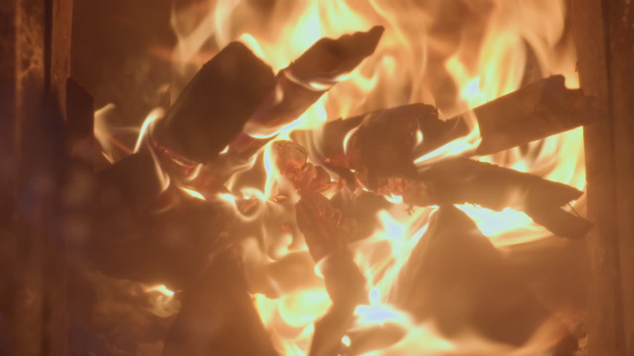 Extreme close up of wood burning fiercely inside chimney. Flames engulf stacked logs, emitting intense heat and vibrant orange glow with visible embers and charred textures in a dramatic fiery scene