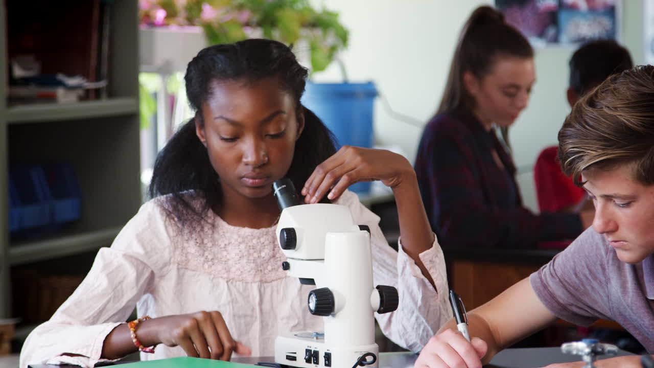 estudiantes de secundaria mirando a través del microscopio y escribiendo notas en la clase de biología