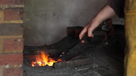 blacksmith stokes a coal fire and pounds a red hot peice of metal with a hammer