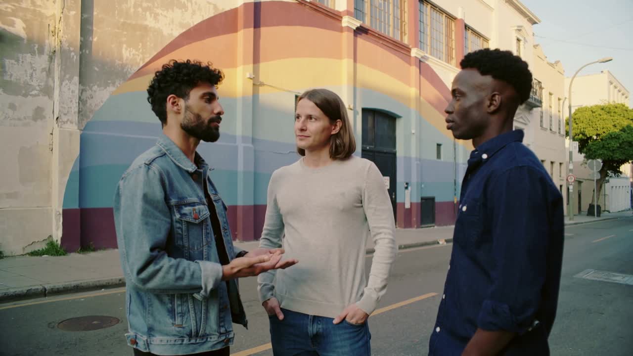 Starting conversation, bearded man in denim sharing story, gesturing to group on street, mural