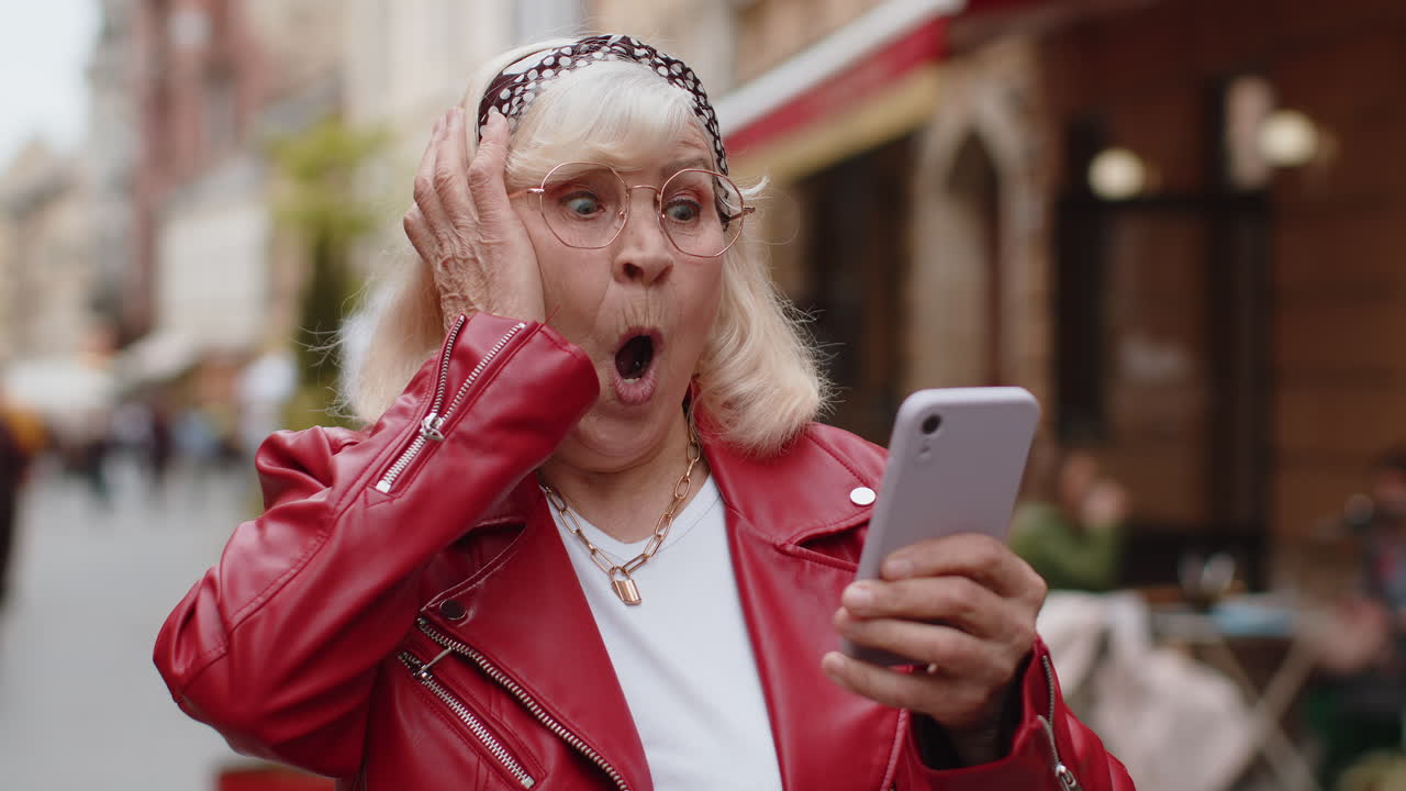 feliz ganadora excitada mujer mayor usa teléfono inteligente celebrando ganar buenas noticias de mensaje en la calle de la ciudad