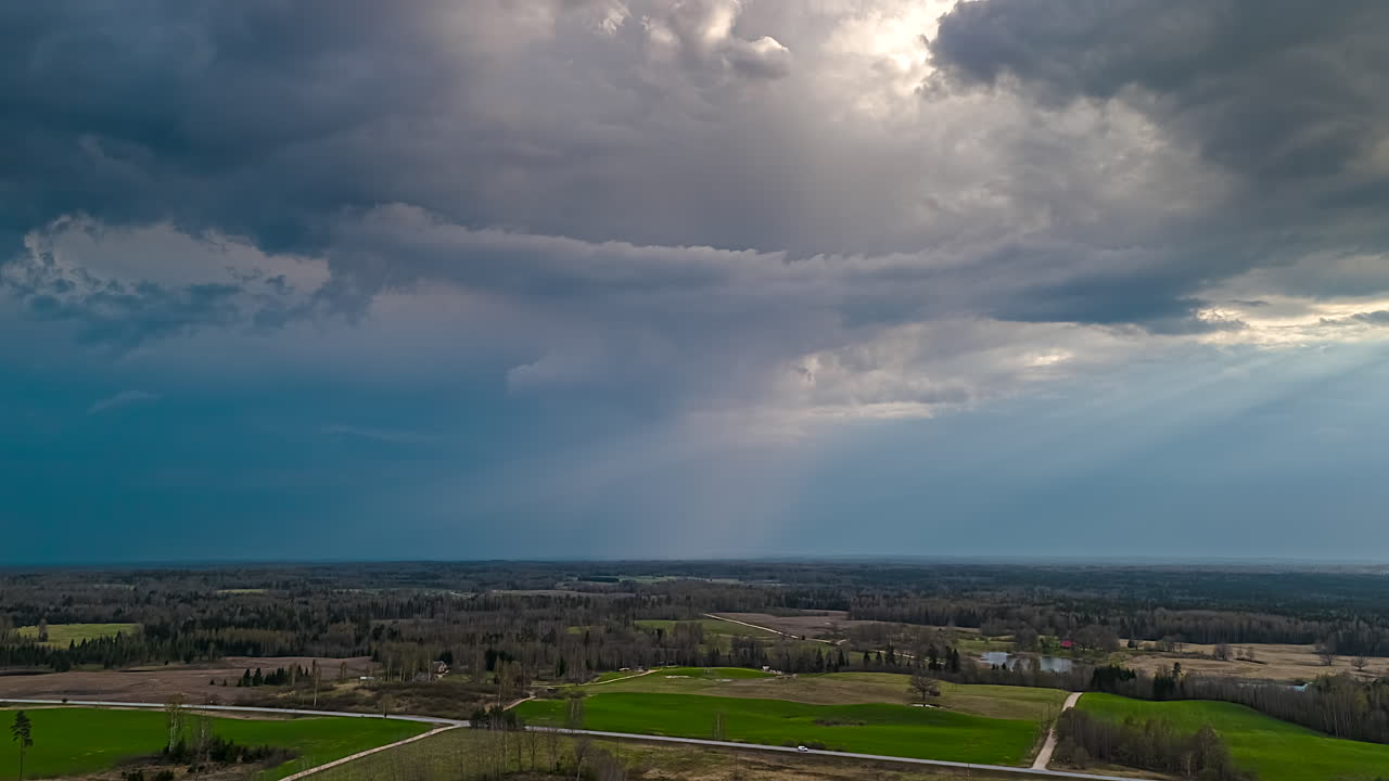 Dark clouds drift by over a green landscape with meadows, forests and roads.