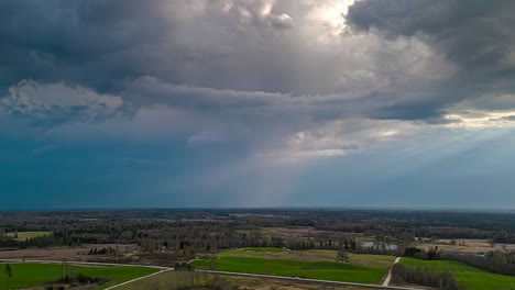 dark clouds drift by over a green landscape with meadows, forests and roads.