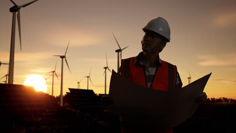 engineer reviewing plans for renewable energy farm at sunset