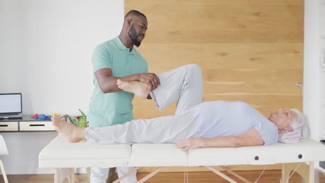 video of african american male physiotherapist exercising with caucasian senior woman