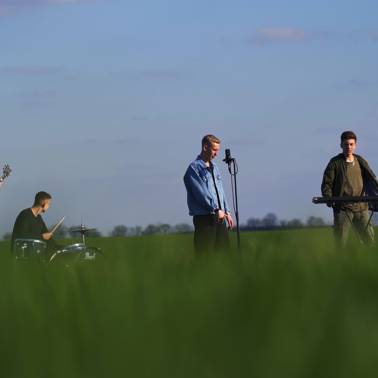 Four men music band sing and play music in the farmlands. Young group making music. Blurred foreground