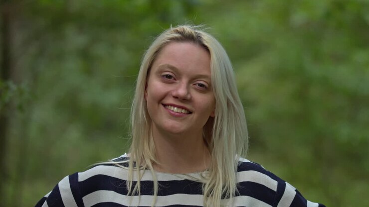 Ritratto di una donna bionda felice e sorridente che guarda la fotocamera. Sfondo con foresta verde naturale. Concetto di sviluppo sostenibile