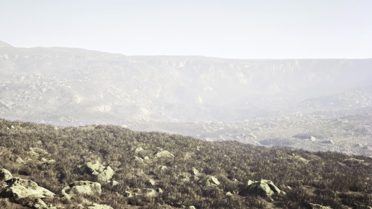 Vast rocky landscape with dry vegetation under a pale sky in daytime