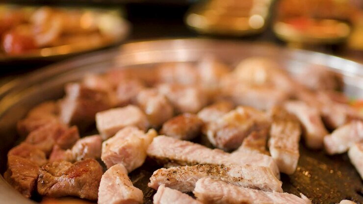 Close-up berbagai macam daging yang dimasak di atas hotplate, dengan uap yang terlihat dan kedalaman bidang yang dangkal