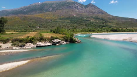 rocky banks of vjosa river with emerald water flowing through green landscape in albania