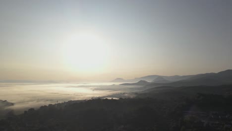 Backwards-dolly-aerial-shot-of-vast-landscape-covered-in-forest-and-mist